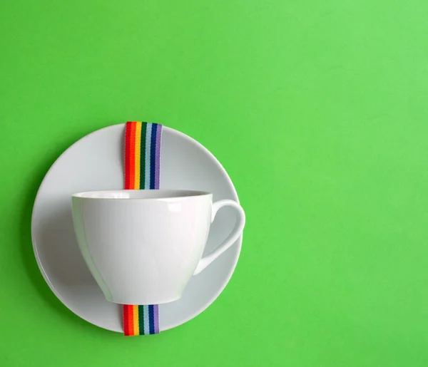 White coffee Cup on green pastel colorful paper geometric flat background with rainbow ribbon lgbt on saucer. Drink Cup template for your design to place text, image and logo layout