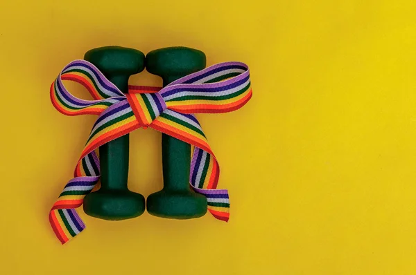 Dos pesas verdes con arco iris de regalo sobre fondo de mesa amarilla, orgullo, deporte y concepto saludable Imagen De Stock
