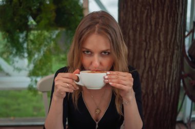 Kafede kahve içen güzel kadın. Bir kafeteryada olgun kadının portresi sıcak kapuçino içme ve kameraya bakarak. Bir fincan kahve ile güzel kadın.