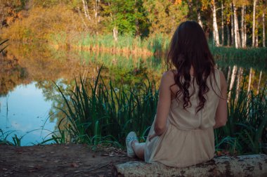 Genç ve çekici bir kadın, göletin kıyısında oturan ve meditasyon, düşünen bir kız. Doğada yalnızlık kavramı
