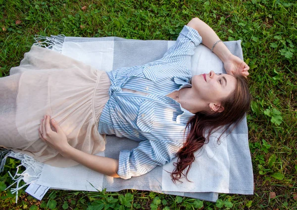 Una mujer en una camisa brillante acostada en la hierba en un parque público y disfruta de su vida de solitudel Fotos De Stock Sin Royalties Gratis