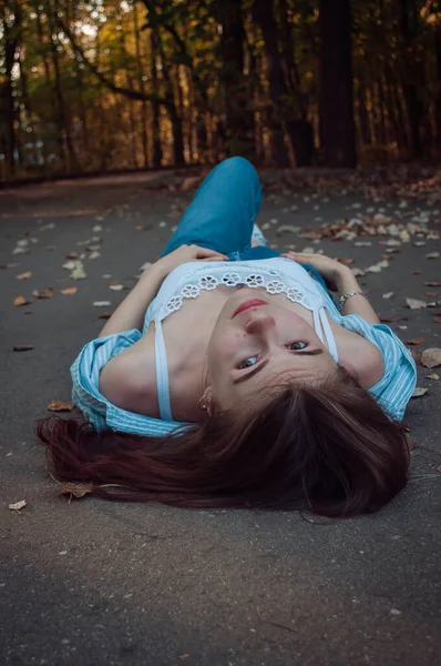 Young beautiful happy girl lying on the road in the Park and smiling. The concept of lifestyle, leisure, relax — Stock Photo, Image