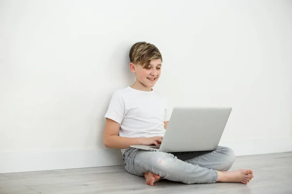 Smiling boy chatting with friends in social networks sitting front laptop .Young boy learning at home during quarantine