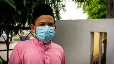 Coronavirus 'ta düzenlenen Bayram kutlamaları sırasında Baju Melayu kumaşı ve Songkok' ta 3 katmanlı maske takan Asyalı genç bir adamın portresi. Hijyen yaşam tarzı. Yeni normal kavram.