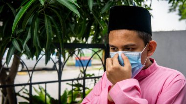 Coronavirus 'ta düzenlenen Bayram kutlamaları sırasında Baju Melayu kumaşı ve Songkok' ta 3 katmanlı maske takan Asyalı genç bir adamın portresi. Hijyen yaşam tarzı. Yeni normal kavram.