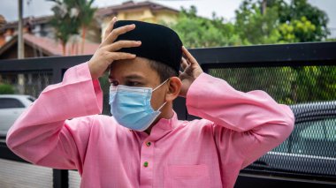 Coronavirus 'ta düzenlenen Bayram kutlamaları sırasında Baju Melayu kumaşı ve Songkok' ta 3 katmanlı maske takan Asyalı genç bir adamın portresi. Hijyen yaşam tarzı. Yeni normal kavram.