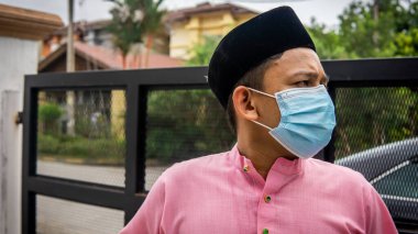Coronavirus 'ta düzenlenen Bayram kutlamaları sırasında Baju Melayu kumaşı ve Songkok' ta 3 katmanlı maske takan Asyalı genç bir adamın portresi. Hijyen yaşam tarzı. Yeni normal kavram.