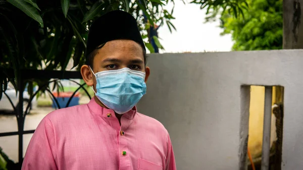 Coronavirus 'ta düzenlenen Bayram kutlamaları sırasında Baju Melayu kumaşı ve Songkok' ta 3 katmanlı maske takan Asyalı genç bir adamın portresi. Hijyen yaşam tarzı. Yeni normal kavram.