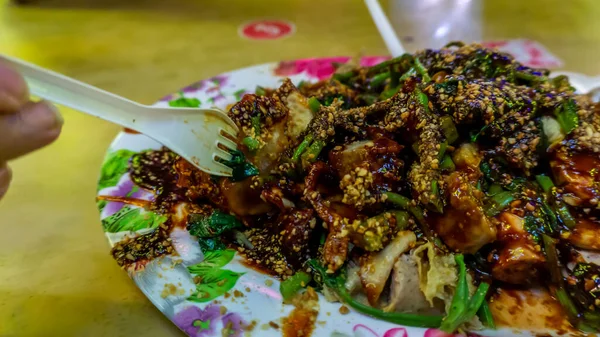 People eating Yong Tau Foo or Yentafu, a Chinese cuisine using plastic fork on a table. Consisting of tofu filled with ground meat mixture or fish paste. Image contain noise and selective focus.