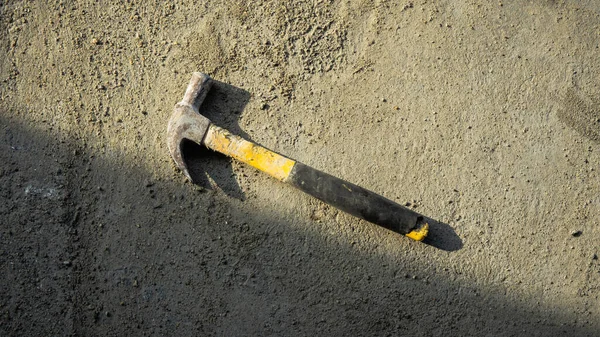 stock image Flat lay of dirty metal hammer on grunge cement background with natural light and shadow. Consist of a weighted head fixed to a long handle that is swung to give an impact to small area of an object.