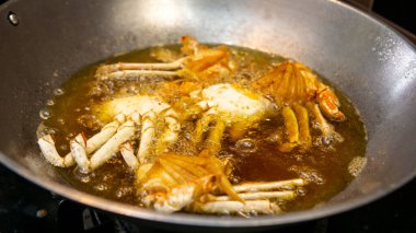 Mutfaktaki metal tavada kızgın yağda kızaran yengecin yakın görüntüsü. Seçici odak.