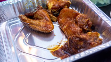 Fırında ızgara yapmadan önce çeşitli baharat ve sosla marine edilmiş çiğ tavuk parçalarını alüminyum bir yiyecek kabında yakından izle..