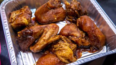 Fırında ızgara yapmadan önce çeşitli baharat ve sosla marine edilmiş çiğ tavuk parçalarını alüminyum bir yiyecek kabında yakından izle..