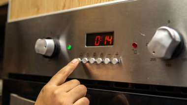 Mutfakta pişirmek için zamanlayıcıyı ayarlayan kız elinin yakın görüntüsü. İstenen zamanı ayarlamak için zamanlayıcı düğmesine tıklanıyor.