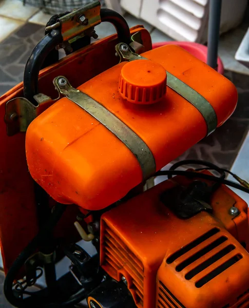 Close up of orange brush cutter machine on the floor. Lawn mower grass trimmer machine body detail.