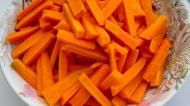 İzole edilmiş beyaz arka planlarda plastik bir bardakta dilimlenmiş çiğ havuç gruplarını yakından izle. Önplana seçici odaklanma.