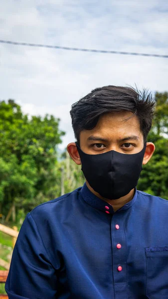 一幅年轻的马来人的画像 他穿着传统的巴朱 梅莱乌布 戴着带有绿色自然背景的黑色织物面罩 防止病毒和疾病传播的防护措施 — 图库照片