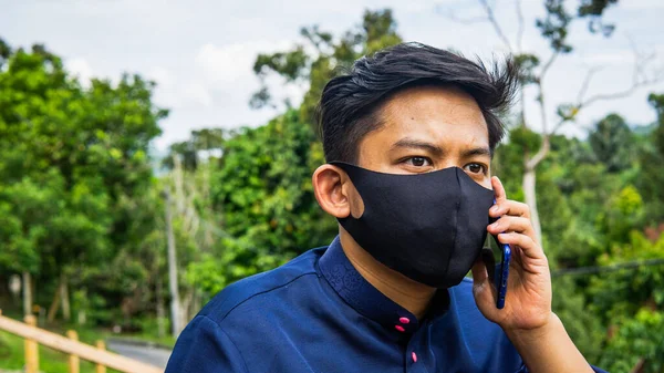 一幅亚洲马来人的画像 身穿巴朱 梅莱乌布 头戴黑色面料面罩 在电话中交谈 卫生生活方式 新的正常概念 — 图库照片