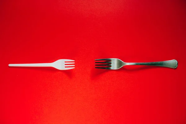 A plastic fork and a metal one on a red background. — Stock Photo, Image