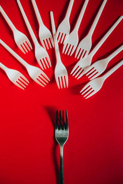 A lot of plastic forks and one metal on a red background.