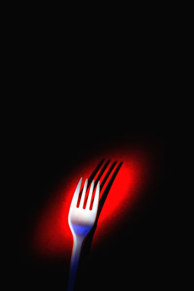 A plastic fork on a red background.