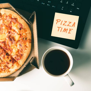 Kutuda pizza, bir fincan kahve, dizüstü bilgisayar ve ofiste Pizza TIME yazılı çıkartma..