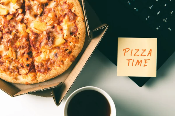Pizza em caixa, xícara de café, laptop e adesivo com texto PIZZA TEMPO na mesa no escritório . Imagens De Bancos De Imagens