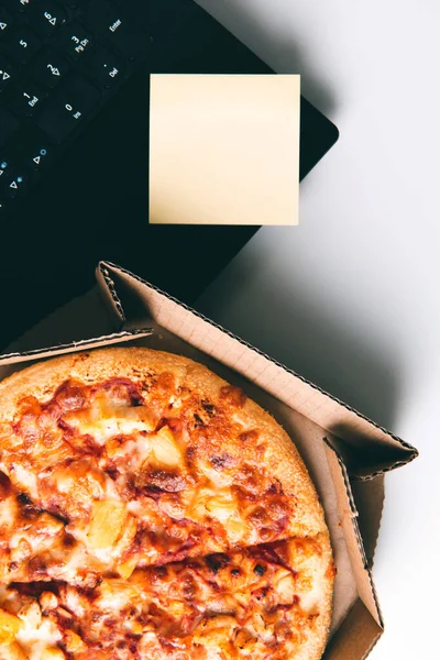 Pizza in box, laptop and empty sticker on table in office. — Stock Photo, Image