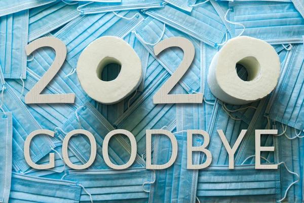 Ιστορικό πολλών ιατρικών μασκών και 2020 GOODBYE λέξεις από λευκούς ξύλινους αριθμούς και γράμματα και χαρτί τουαλέτας. — Φωτογραφία Αρχείου