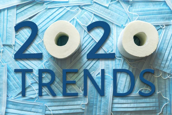 Background of a lot of medical masks and TRENDS 2020 words from blue wooden numbers and letters and toilet paper.