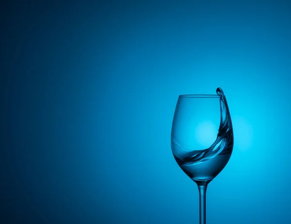 水のガラスが青い背景にガラス中の水の青い Background Splash のアクリル ガラスの上に立つ — ストック写真