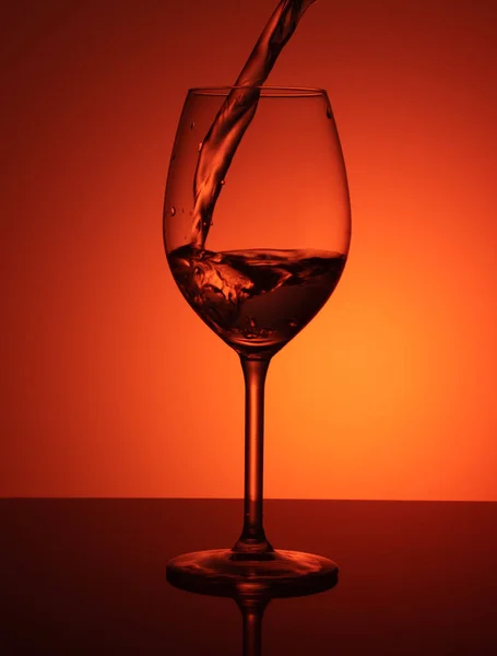 オレンジ色の背景にガラス中の水のスプラッシュ オレンジ色の背景上に水のガラス — ストック写真
