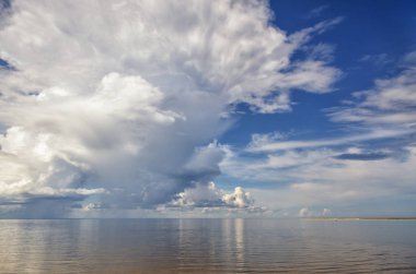 Mavi gökyüzüne karşı denizin üzerinde beyaz gök gürültüsü bulutları