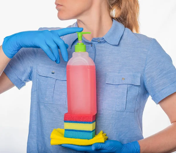 Mujer en uniforme azul y guantes de nitrilo sosteniendo productos de limpieza delante de ella —  Fotos de Stock