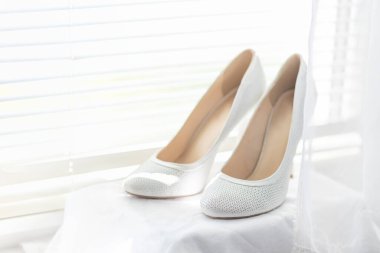 Gelin için beyaz ayakkabılar perdelerin arkasında pencere eşiğinde duruyor.