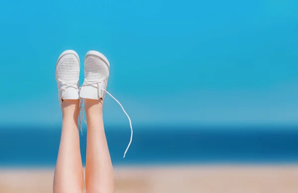 Женские ноги на пляже подняты на фоне моря в белых кроссовках. Изображение слева. пространство для текста справа . — стоковое фото