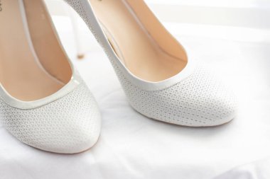 Gelin için beyaz ayakkabılar. Arka planda parlak bir pencere ve külüstür jaluzi.