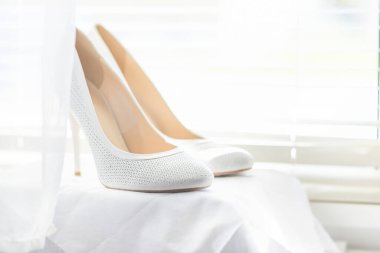 Jaluzili parlak bir pencerenin arkasında gelin için beyaz ayakkabılar var.