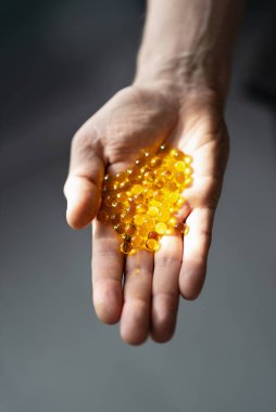 Şeffaf kapsüllerdeki sarı keten tohumu yağı gri arka planda bir elde bulunur. sağlıklı besin takviyesi