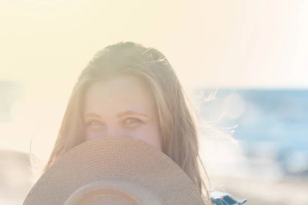 Koncepcja spokoju umysłu i szczęścia. Kobieta w blond włosach w słomkowym kapeluszu i dżinsowej kurtce stoi na tle morza i cieszy się słońcem. — Zdjęcie stockowe