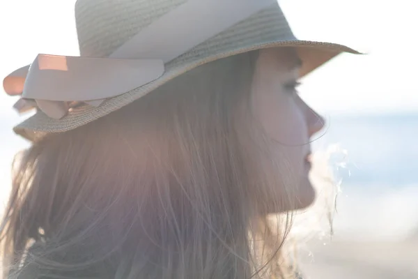 Koncepcja spokoju umysłu i szczęścia. Kobieta w blond włosach w słomkowym kapeluszu i dżinsowej kurtce stoi na tle morza i cieszy się słońcem. — Zdjęcie stockowe