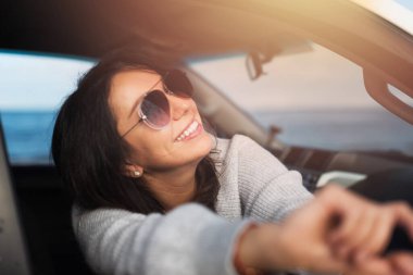 Mavi denizin arka planında beyaz bir arabanın penceresinden gülümseyen mutlu genç esmer..