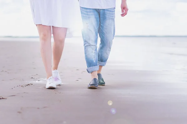 Pernas masculinas e femininas em calçados esportivos caminham ao longo da praia contra o fundo do mar. — Fotografia de Stock