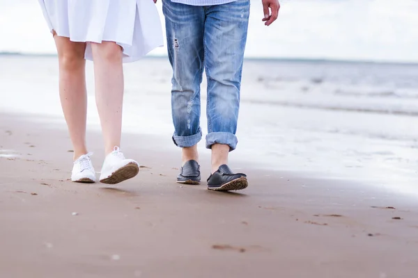 Piernas masculinas y femeninas en zapatos deportivos caminan a lo largo de la playa contra el fondo del mar. — Foto de Stock