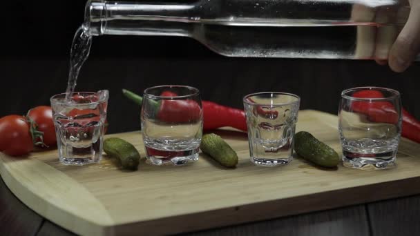 Pour vodka into shot glasses placed on a wooden board — Stock Video