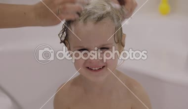 Çekici üç yaşında kız banyo yapsın. Anne bir şampuanla temiz saç. Sevimli sarışın çocuk. Kahverengi gözler. Kız saçını yıkamak gibi değil. Küçük çocuk, 3-4 yaşında sarışın kız