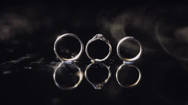 結婚指輪と婚約指輪の光で輝いている暗い水面に横になっているマクロを閉じます — ストック動画