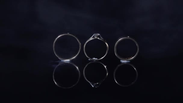 結婚指輪と婚約指輪の光で輝いている暗い水面に横になっているマクロを閉じます — ストック動画