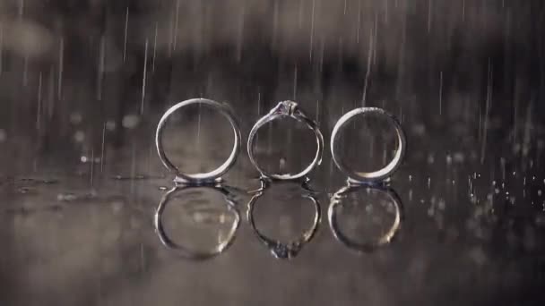 结婚戒指和订婚戒指躺在黑暗的水面上 闪耀着明亮的宏观 水溅起 慢动作 — 图库视频影像