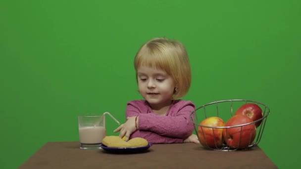 Lány ült az asztalnál és eszik, csoki, süti, alma. Boldog három éves lány. Aranyos lány mosolyogva. Szép kis gyermek, 3-4 éves szőke lány. Hogy arcok. Zöld képernyős videó. Chroma Key